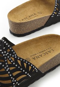 Zwarte slipper met uitsnijdingen, versierd met rhinestones, kurken voetbed en een gestructureerde zool. Logo gedrukt op de beige binnenzool.