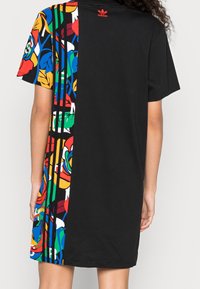 Černé šaty v tričkovém stylu s barevnými květinovými vzory na jedné straně, krátkými rukávy a červeným logem na zadním výstřihu.