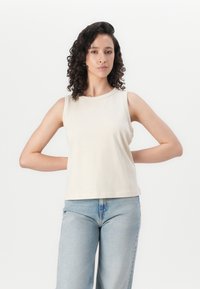 Top sin mangas beige hecho de una tela suave, con un escote redondo y un corte relajado, combinado con unos pantalones vaqueros de talle alto en azul claro.