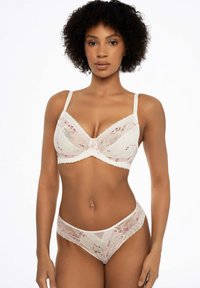 Koronkowy komplet bielizny w kolorze kości słoniowej, z różowymi kwiatowymi akcentami. Białe biustonosze z fiszbinami i falbaniastymi krawędziami; pasujące stringi dopełniają cały wygląd.