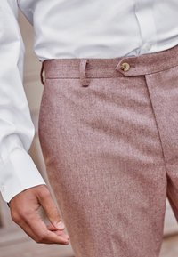 Helle rosa, strukturierte Hose mit Knopfverschluss, Gürtelschlaufen und tailliertem Schnitt, kombiniert mit einem weißen Hemd.