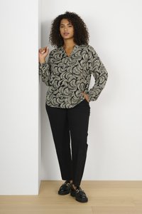 Schwarze Bluse mit cremefarbigem Blättermuster, langen Ärmeln und lockerer Passform, kombiniert mit maßgeschneiderten schwarzen Hosen und klobigen schwarzen Schuhen.