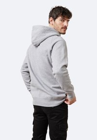 Sudadera gris con capucha ajustable, puños y dobladillo acanalados. Cuenta con un bolsillo canguro y una pequeña etiqueta de logo en el lado.