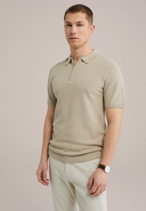 Beige Poloshirt mit kurzem Arm, Reißverschluss und Kragen, strukturiertes Strickmuster, kombiniert mit hellen Hosen und einer braunen Uhr.