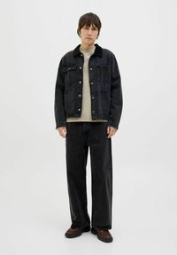 Black denim jacket with four pockets, button closure, and a soft collar, worn over a striped beige shirt and black wide-leg jeans. Brown shoes.
