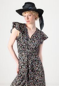 Robe florale noire avec des fleurs roses et bleues, manches courtes froncées, décolleté en V, taille cintrée et un chapeau noir à large bord assorti avec un ruban.