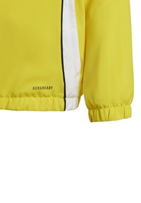 Giacca gialla leggera con striscia bianca ai lati e finiture nere. Presenta polsini elasticizzati e logo "AEROREADY" nell'orlo.