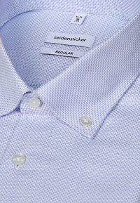 Chemise habillée bleu clair avec petit motif en zigzag, boutons blancs et étiquettes indiquant "seidensticker," "REGULAR," et taille "15 1/2 M 39."