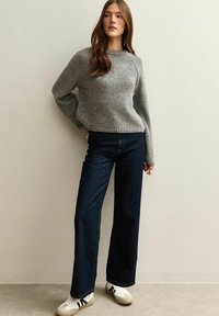 Grijze gebreide trui met een ronde halslijn, relaxte mouwen, gecombineerd met donkerblauwe wijde jeans en witte sneakers met zwarte strepen.