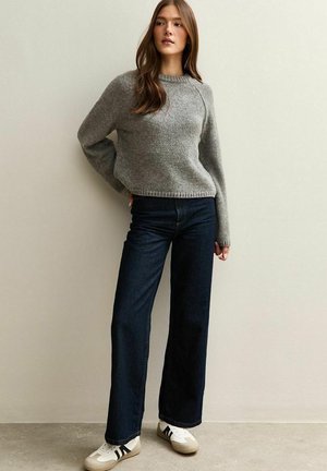 Grijze gebreide trui met een ronde halslijn, relaxte mouwen, gecombineerd met donkerblauwe wijde jeans en witte sneakers met zwarte strepen.