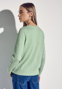 Ljust grönt ribbat tröja med långa ärmar, rund halsringning och en avslappnad passform, parat med blå denimjeans.