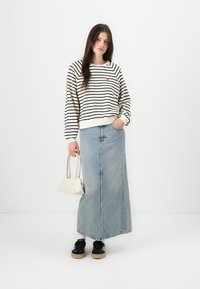 Stripet, krem genser med rødt hjerte detaljer, kombinert med en lys denim maxiskjørt, svarte sko og en liten hvit håndveske.