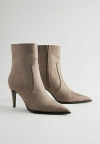 Botine din suede bej, cu vârful ascuțit și toc stiletto de 8 cm. Prezintă un fermoar pe lateral și o textură netedă.