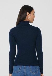 Pull à col roulé côtelé bleu marine avec des manches longues. Texture douce et coupe ajustée, porté avec un jean en denim taille haute.