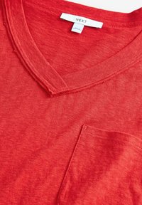 Rød bomulds t-shirt med V-hals design, der har en brystlomme og subtil struktur. Etiketten siger "NEXT."