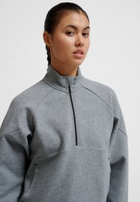 Felpa grigia con zip e colletto alto, caratterizzata da una zip a metà e maniche raglan. Texture morbida e design minimalista senza pattern.