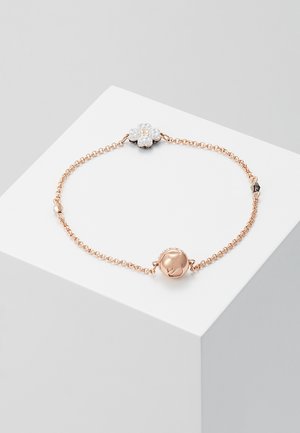 Bracelet délicat en chaîne en or rose avec un charm floral en cristal blanc et un charm sphérique en or rose sur une plateforme blanche.