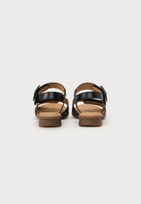 Black leather sandals with a rectangular buckle, open toe design, non-slip brown sole, and a low heel. Textured insole for comfort.