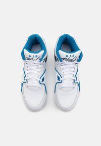 Pár bílých a tyrkysových tenisek Nike Air Flight s bílými tkaničkami, viděné zhora na bílém pozadí.