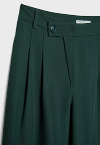 Dunkelgrüne, plissierte Hose aus glattem Stoff mit einem einfachen Knopfverschluss am Bund und Gürtelschlaufen.