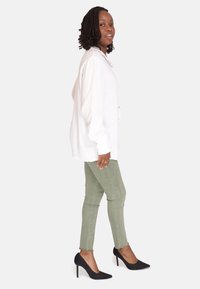 Hvid skjorte med lange, puffede ærmer, parret med olivengrønne skinny jeans og sorte stilettohæle. Lys baggrund.
