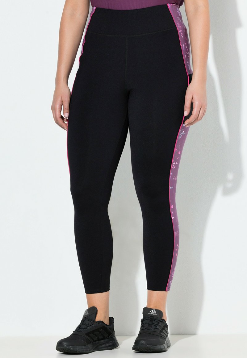 Zwarte sportlegging met hoge taille, voorzien van roze bloemen zijpanelen en gestructureerde accenten. Gemaakt in combinatie met zwarte sportschoenen.