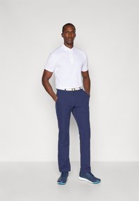 Hvit polo skjorte med korte ermer og knapplist; marineblå bukser med en glatt tekstur; blå treningssko med hvite såler.