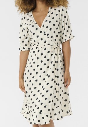 Sukienka kopertowa z kremowej tkaniny w czarne akwarelowe groszki. Posiada krótkie rękawy, pasek do wiązania oraz rozszerzany dół. Gładka faktura.