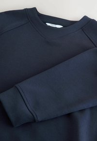 Dunkelmarineblaues Langarm-Sweatshirt mit V-Ausschnitt und gerippten Bündchen, flach ausgelegt mit einem Ärmel über den Körper gefaltet.