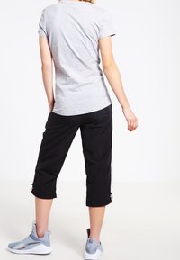 Szara koszulka z krótkim rękawem zestawiona z czarnymi spodniami o krótszej długości. Spodnie mają sznurek u dołu i są uzupełnione szarymi butami sportowymi.