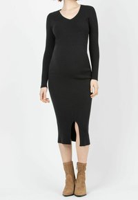 Robe en tricot côtelé noir avec de longues manches, décolleté en V et fente sur le côté à l'ourlet. Portez-la avec des bottes chevilles en suède beige.