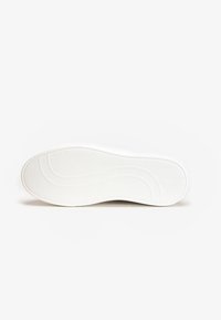 Valkoinen lenkkarin pohja, jossa on sileä pinta ja teksturoitu pito-kuvio. Mukana kaarevat viivat ja hienovarainen aaltoilu.