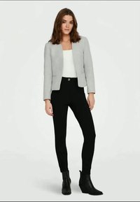 Veste cropped gris clair sur un haut blanc, associée à un pantalon noir ajusté et des bottines. Texture lisse avec un minimum de détails.