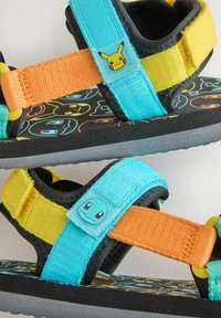 Barnsandaler med färgglada vävda remmar i blått, gult och orange, med lekfulla motiv av Pikachu och Squirtle på justerbara stängningar.