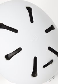 Hvit hjelm med ventilasjonsåpninger, sirkulær form og en jevn overflate. Har preget logo og svarte detaljer rundt åpningene.