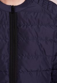 Navy puffer jacket featuring a zipper closure, horizontal quilted pattern, ribbed accents at shoulders, and a smooth fabric texture.