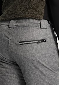 Pantalons en tissu gris avec une poche arrière zippée dotée d'un zip noir contrastant. Le matériau présente une apparence texturée et chinée.