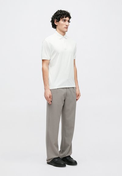 Bílá polokošile s krátkými rukávy a límečkem, doplněná o světle šedé, volné kalhoty a černé tenisky. Jednoduchý design bez vzorů.