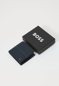 Marine lærveske med teksturert stripedesign, med en kompakt form. Leveres med en svart boks merket "BOSS" i hvitt.