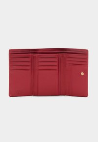Punane nahast rahakott, millel on mitu kaardipesa, münditasku ja klõpsuga sulgur. Omab reljeefset logo ja siledat tekstuuri.