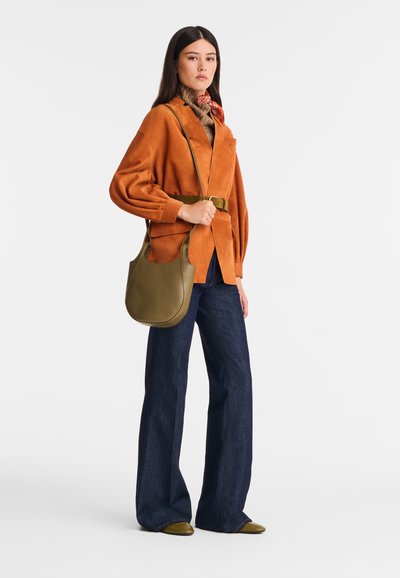 Gebranntes orangefarbenes Wildlederjackett, marineblaue Schlagjeans, olivgrüne Lederhandtasche und ein gemusterter Schal. Glatte Texturen und entspannter Schnitt.