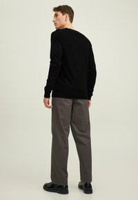Pullover nero con maniche lunghe, scollatura rotonda e una texture liscia, abbinato a pantaloni grigi a vestibilità larga e scarpe stringate nere.