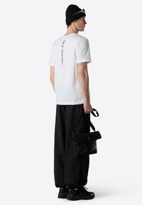 Hvid bomulds t-shirt med trykt tekst på ryggen, parret med sorte cargo bukser og en sort taske med en strop og hardware detaljer.