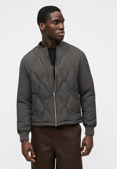 Chaqueta bomber gris acolchada con cuello alto, cremallera frontal, puños acanalados y un diseño ligeramente cropped, usada sobre una camiseta negra.