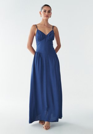 Tyrkysově modrá maxi šaty s tenkými ramínky, přiléhavou tělnou částí a splývavou sukní; hladká textura s jemným leskem.