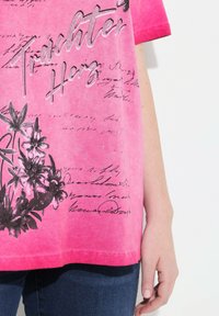 Camiseta de manga corta rosa con gráficos florales en negro y texto escrito a mano, acentuada con rhinestones para un detalle adicional.