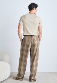 Beige cotton t-shirt and brown plaid lounge pants with an elastic waistband, featuring a relaxed fit and side pockets, worn barefoot.