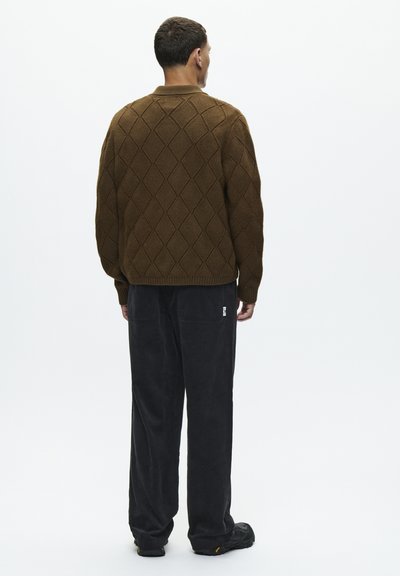 Pull en tricot marron avec un motif en losanges, associé à un pantalon en velours côtelé noir. Le haut présente un col et des poignets côtelés.