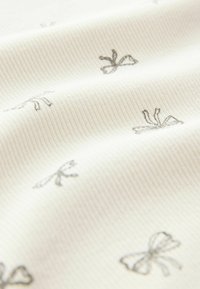 Ribbed fabric in off-white featuring a pattern of small grey bows. The texture appears soft and slightly stretchy.