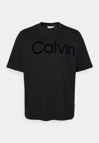 Camiseta de algodón negra con un gran logo en relieve tonal "Calvin" en el pecho. Cuello redondo y mangas cortas, textura suave.
